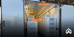 Cửa kho mở ra để lộ một chồng thùng hàng logistics cùng hệ thống camera giám sát.