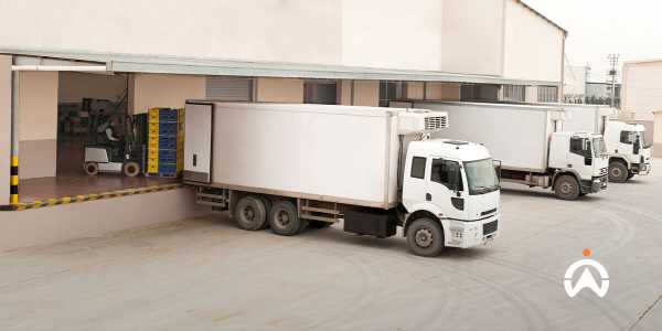 Ba xe tải giao hàng màu trắng tại bến bốc dỡ đang được dỡ hàng bằng xe nâng.